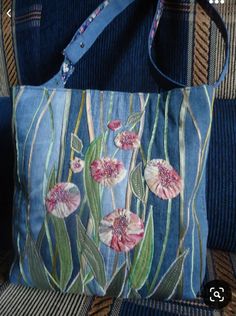 a blue purse with pink flowers on it sitting on a couch next to a handbag