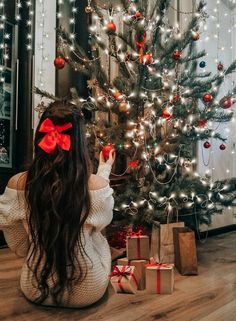 a woman sitting in front of a christmas tree