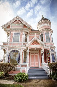 a pink victorian house with white trim and windows on the front porch, stairs leading up to the second floor