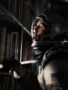 a man in a space suit is holding a book and looking at the bookshelf