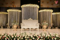 a white couch sitting on top of a stage covered in flowers and greenery next to gold vases