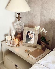 a small table with a lamp, photo frame and flowers on it