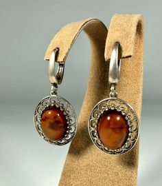 Elevate your style with our Handmade Earrings featuring spectacular orange amber set in textured 925 sterling silver. These exquisite earrings are designed for women who appreciate unique and original jewelry. The vibrant orange amber stones are beautifully complemented by the textured silver, creating a stunning and eye-catching piece that adds a touch of elegance and sophistication to any outfit. Product Details: Material: 925 Sterling Silver Stone: Orange Design: Textured Silver with Unique S Elegant Amber Sterling Silver Earrings, Amber Sterling Silver Dangle Earrings, Classic Amber Sterling Silver Earrings, Amber Sterling Silver Earrings, Silver Baltic Amber Earrings, Elegant Amber Earrings With Polished Finish, Amber Dangle Earrings For Anniversary, Amber Dangle Earrings For Formal Occasions, Vintage Amber Dangle Earrings