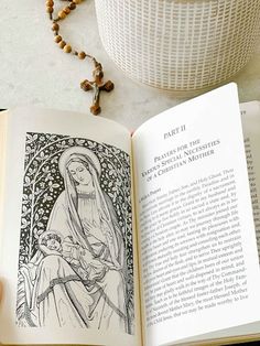 an open book on a table next to a rosary and a vase with flowers in it