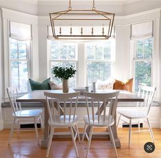 a dining room table with four chairs and a bench in front of the window,