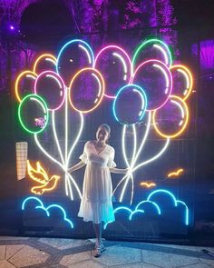 a woman standing in front of a display of balloons and flowers with lights on it