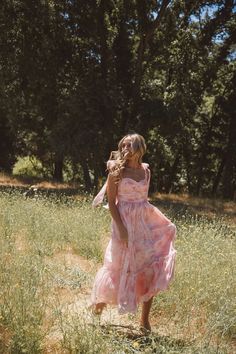 a woman in a pink dress is walking through the grass