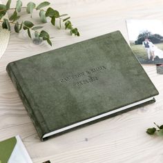 a green wedding album on a table next to some flowers and other personalized items