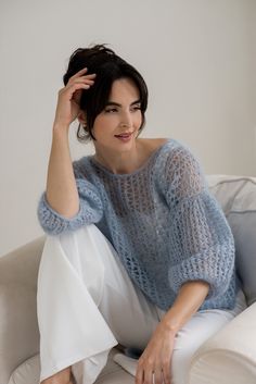 a woman sitting on top of a white couch wearing a blue sweater and white pants