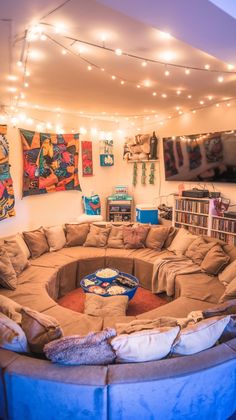 a living room filled with lots of couches and bookshelves under string lights