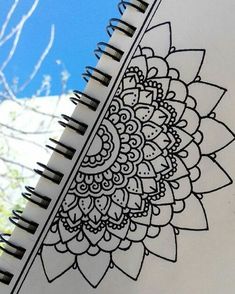 an open spiral notebook with black and white designs on the cover, next to a tree