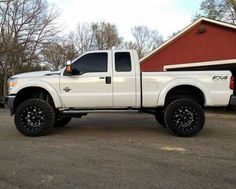 a white truck parked in front of a red barn with black tires and rims