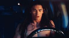 a shirtless man driving a car in the dark