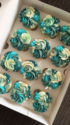 twelve cupcakes in a box with blue and white frosting on the top