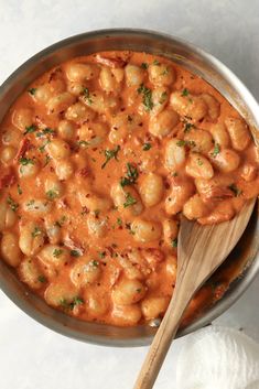 a pot filled with pasta and sauce on top of a white tablecloth next to a wooden spoon