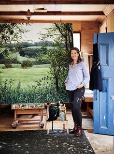 a woman standing next to a painting in a room with blue doors and wooden floors