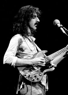 a man with long hair playing an electric guitar in front of a microphone on stage