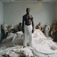 a man standing on top of a bed covered in white sheets and cloths, surrounded by statues