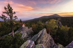 the sun is setting in the distance over some rocks with trees on them and mountains in the background