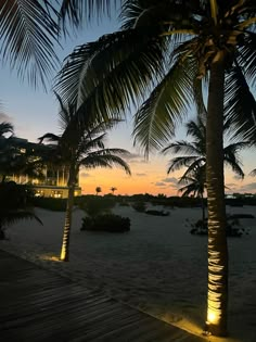 the sun is setting behind two palm trees on the beach in front of a hotel