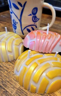 three candles sitting on top of a wooden table next to a cup and saucer