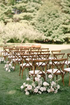 rows of wooden chairs with white flowers on them in front of some trees and bushes