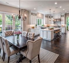 a large dining room table and chairs in front of an open kitchen with white cabinets