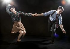 two people are dancing in the dark with their arms extended and one is wearing a tie