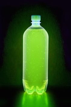 a green bottle with liquid in it on a dark surface, lit up by the light from below