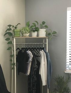 a rack with clothes and plants on top of it in a room next to a window