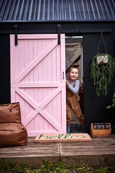 a little boy standing in front of a pink barn door with his hands on the window