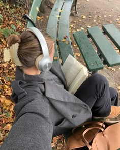 a woman is sitting on a bench with headphones and reading a book while listening to music