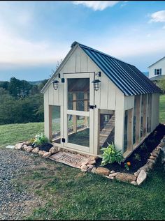 a small chicken coop in the middle of a field with grass and rocks around it