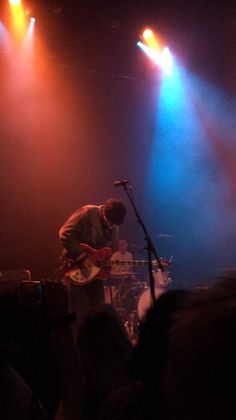 a man playing guitar in front of a crowd at a concert with bright colored lights