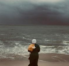 a person standing on the beach looking out at the ocean with an umbrella over their head