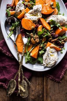 a white plate topped with salad next to two spoons on top of a wooden table