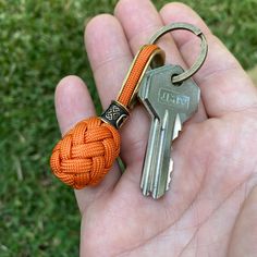 a hand holding two keys with an orange knot on it's end and a gold colored keychain