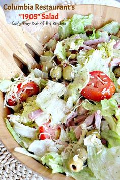 a salad with tomatoes, lettuce and olives in a wooden bowl