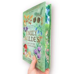 a hand holding up a green book with flowers and plants on it