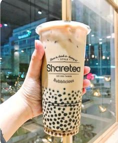 a person holding up a cup of bubble tea in front of a window with the words sharetea written on it