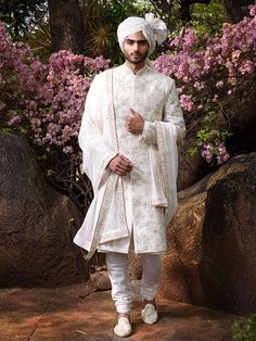 a man in a white outfit standing next to some rocks and pink flowers on the ground