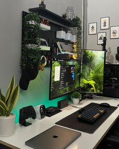 a desk with a laptop, monitor and keyboard sitting on top of it next to a potted plant