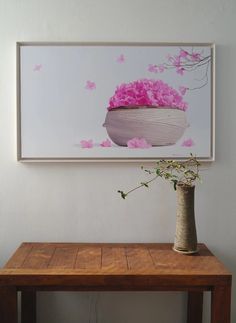 a vase filled with pink flowers sitting on top of a wooden table next to a painting