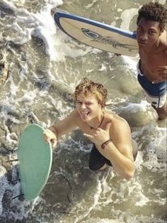 two men are in the water with surfboards and one is holding a green frisbee