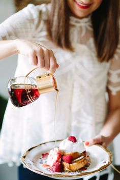 a woman pouring syrup on some french toast with strawberries and whipped cream in a plate