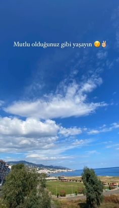 there is a blue sky with white clouds and some trees in front of the water