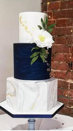 a three tiered white and blue wedding cake on top of a table with flowers