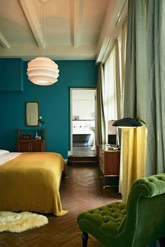 a bed room with a neatly made bed next to a green chair and a window