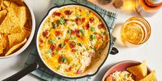 a casserole dish with cheese, bacon and green onions next to some tortilla chips