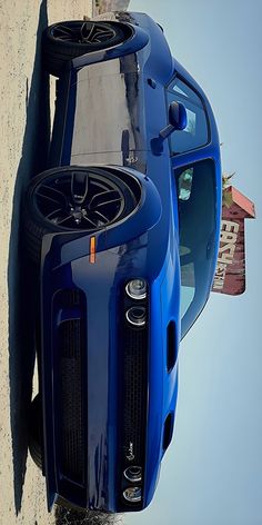 the front end of a blue sports car parked next to a wall with a building in the background